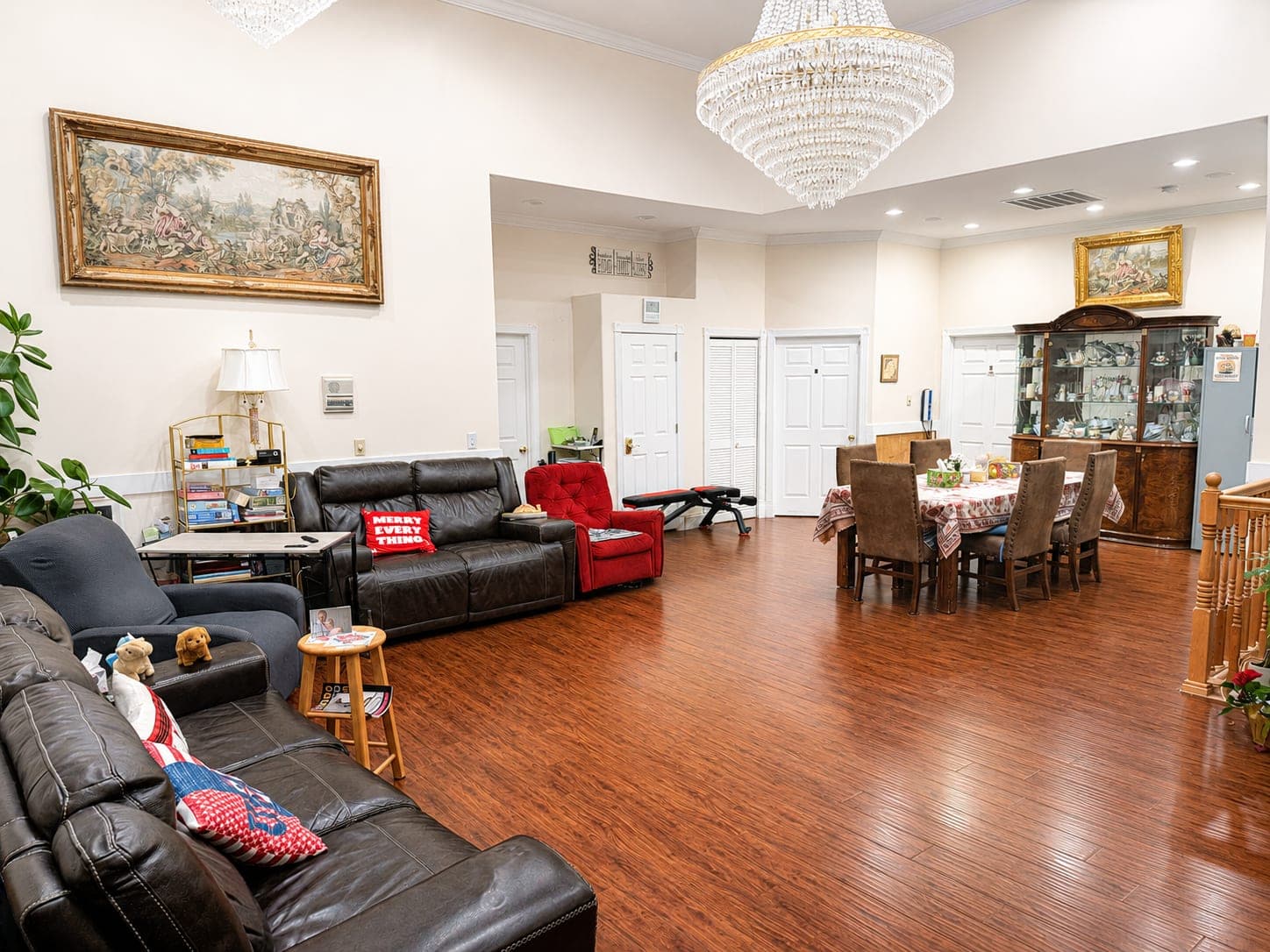The shared living room, with sofas and armchairs on a wood floor beneath a chandelier, and the dining table beyond.